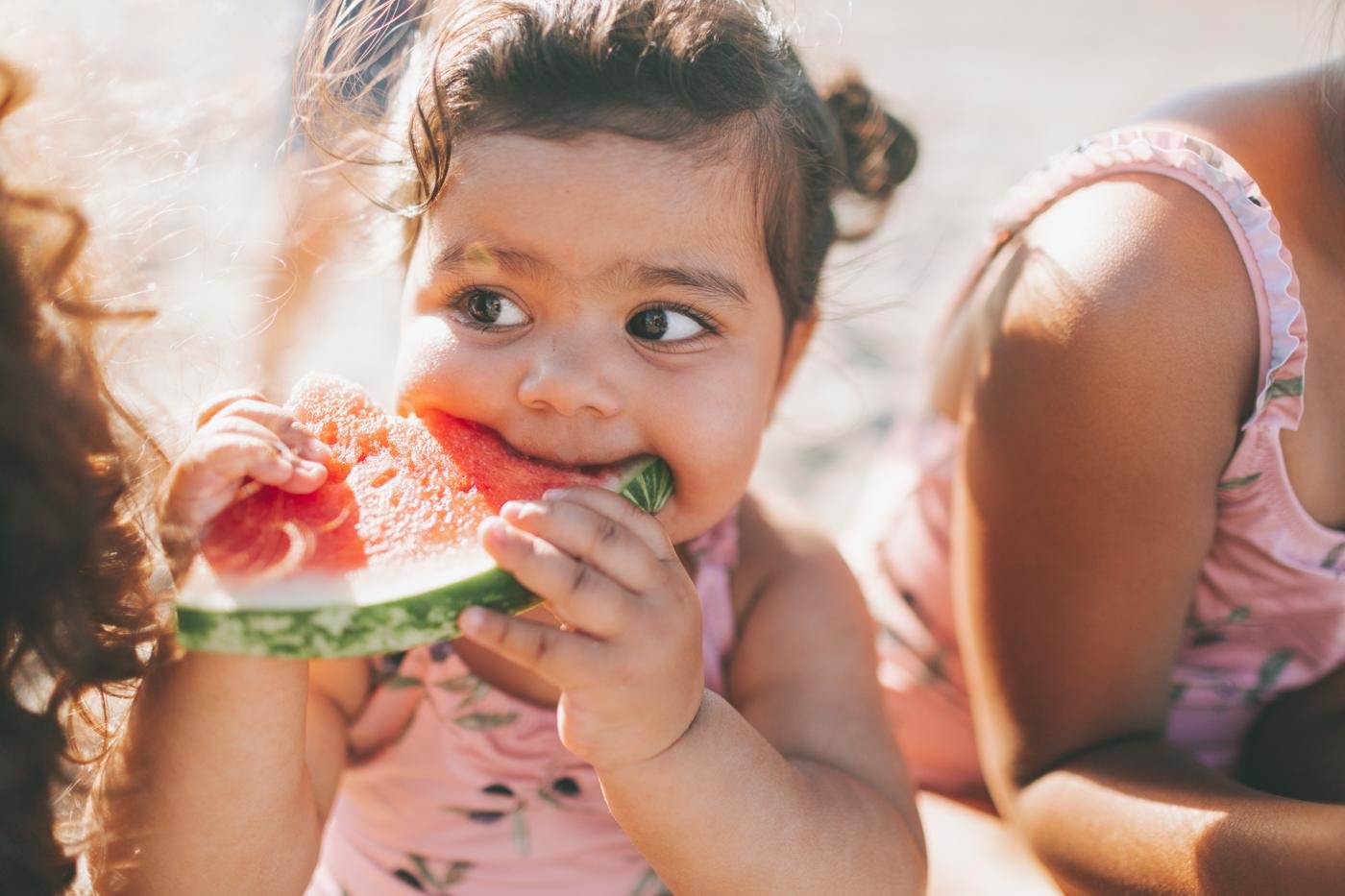 A baby happily eating a slice of watermelon outdoors