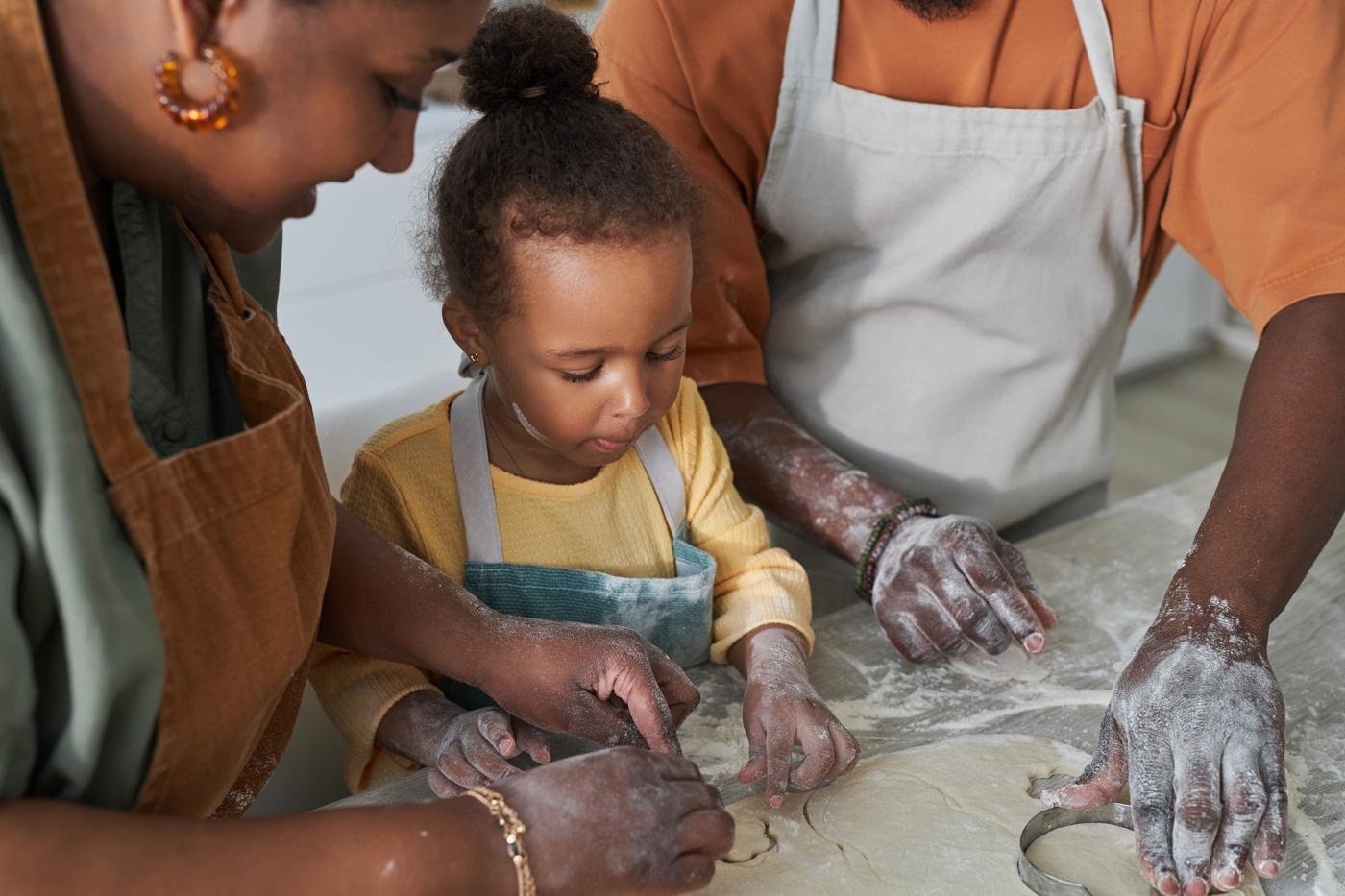 Parents guiding a young child as she explores dough with her hands at the kitchen counter