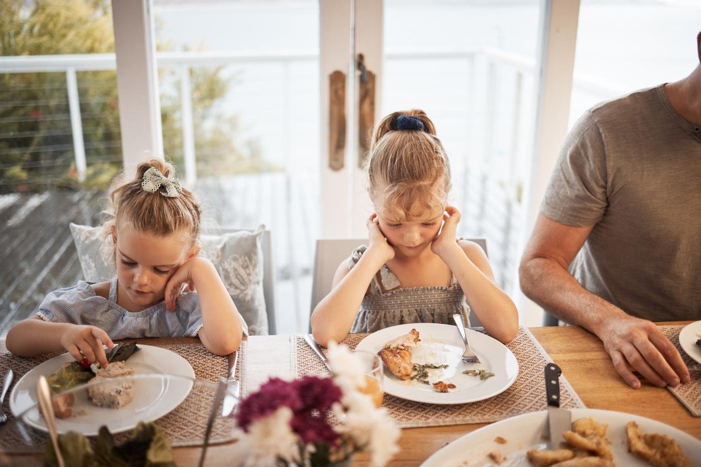 Two young children sitting at a family dinner table, disengaged from their plates