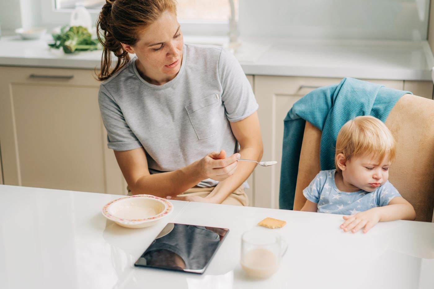 A parent offering a spoon to a toddler who turns away from the food
